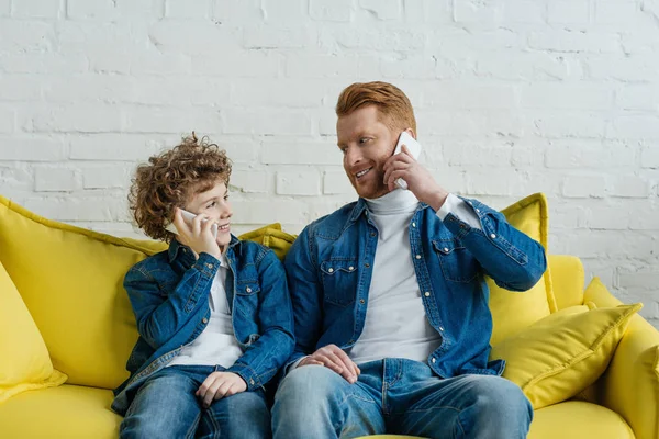 Father and son talking on smartphones while sitting on sofa — Stock Photo