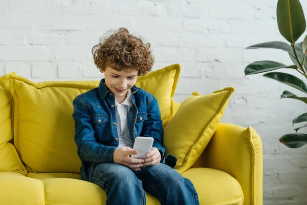 Kind schaut auf Handy, während es auf Sofa sitzt — Stockfoto