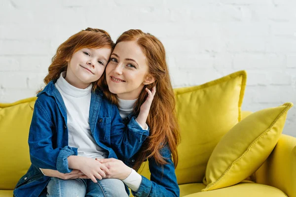 Рыжая женщина обнимает свою дочь на диване — стоковое фото