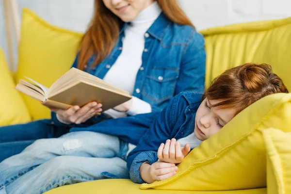 Mère lecture livre pour dormir fille sur canapé jaune — Photo de stock