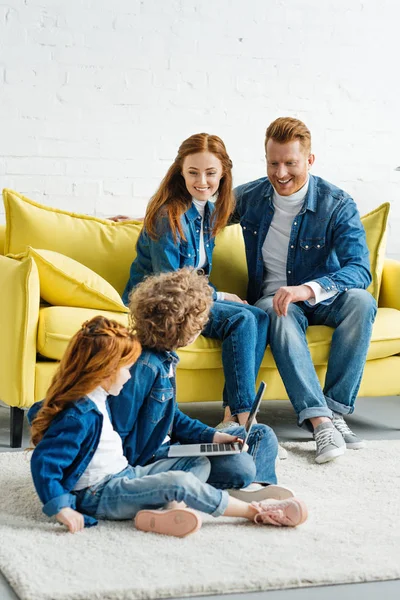 Kinder benutzen Laptop, während Eltern auf dem Sofa sitzen — Stockfoto