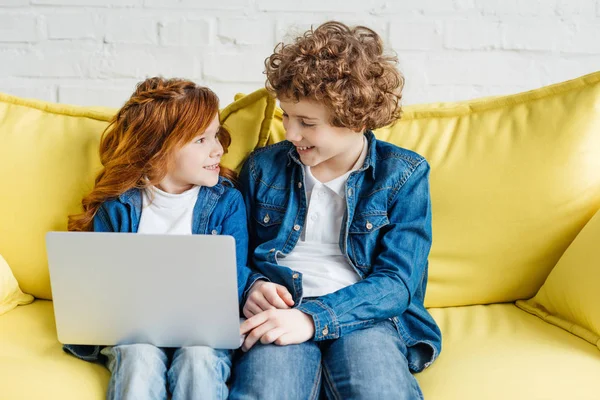 Lindos niños usando el ordenador portátil mientras están sentados en el sofá - foto de stock