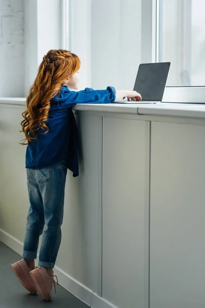 Niño adorable llegar a la computadora portátil en el alféizar de la ventana - foto de stock