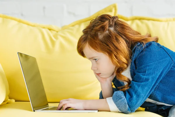 Cute redhead child using laptop on sofa — Stock Photo