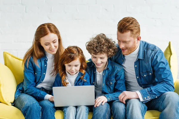 Redhead family sitting on sofa and looking at laptop screen — Stock Photo