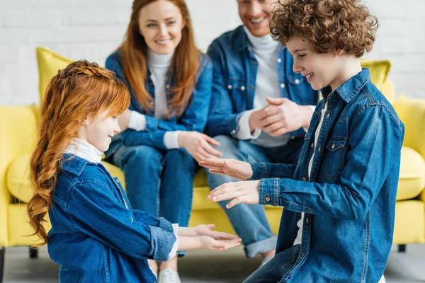 Sonriendo a los niños jugando mientras los padres se sientan en el sofá - foto de stock