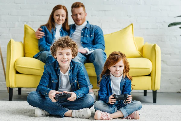 Kinder spielen Videospiel, während Eltern auf dem Sofa sitzen — Stockfoto