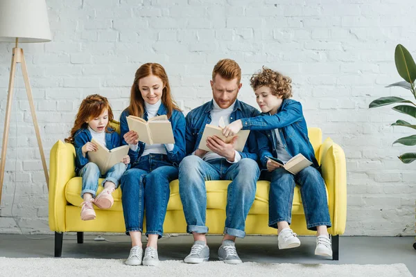 Padres e hijos sentados en un sofá y leyendo libros - foto de stock