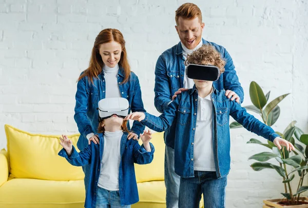 Niños usando anteojos vr de pie frente a sus padres sonrientes - foto de stock