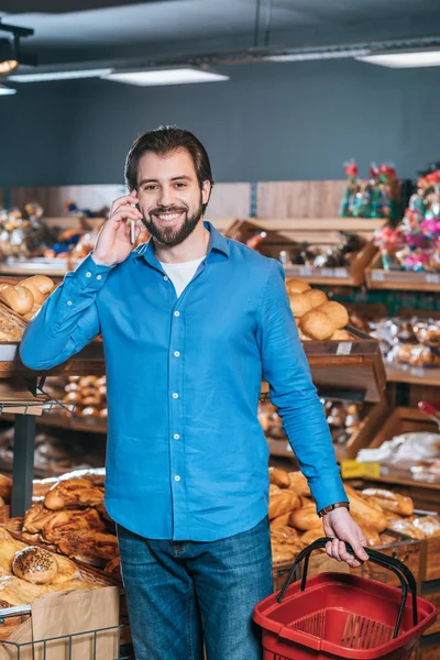 Retrato de comprador sonriente hablando en smartphone en tienda de comestibles - foto de stock