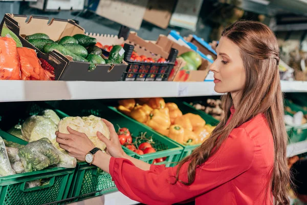 Vista lateral de la mujer que elige verduras frescas crudas en la tienda de comestibles - foto de stock