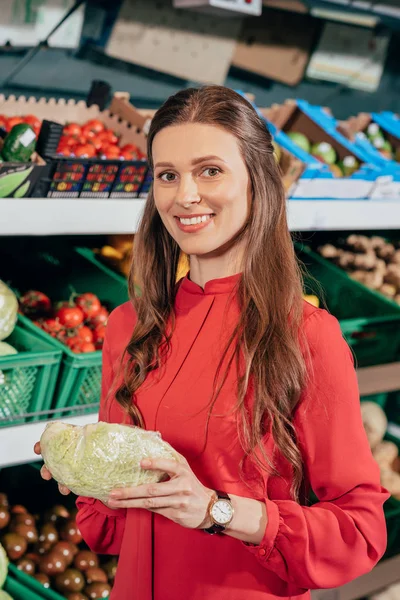 Портрет усміхненої жінки, яка вибирає свіжі сирі овочі в продуктовому магазині — стокове фото