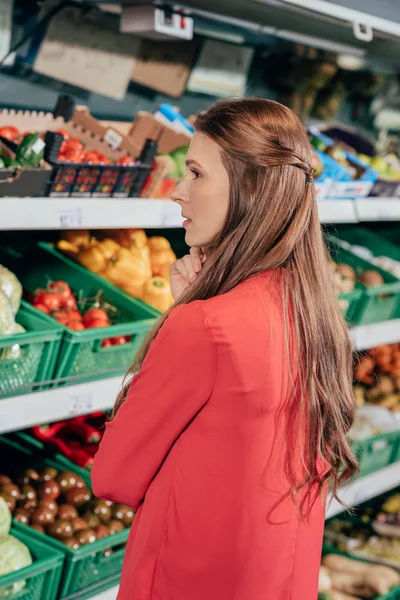 Vista lateral de la mujer que elige verduras frescas crudas en la tienda de comestibles - foto de stock