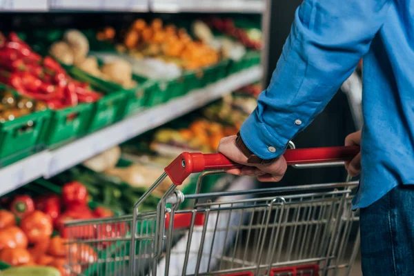 Tiro recortado del hombre con carrito de la compra en la tienda de comestibles - foto de stock