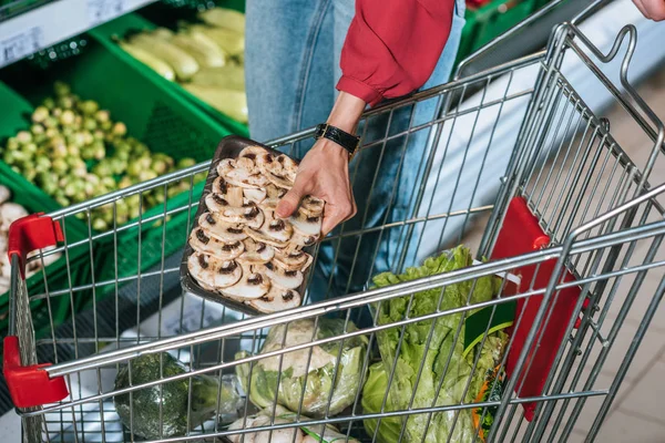 Vista parcial del comprador poniendo productos en el carrito de la compra en el supermercado - foto de stock