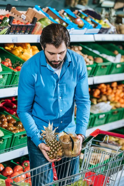 Retrato del hombre poniendo frutas en el carrito de la compra en la tienda de comestibles - foto de stock