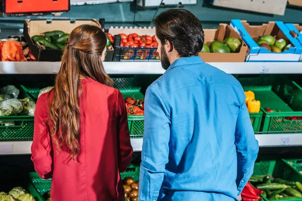 Vista trasera de la pareja con cesta de la compra elegir verduras frescas juntos en el supermercado - foto de stock