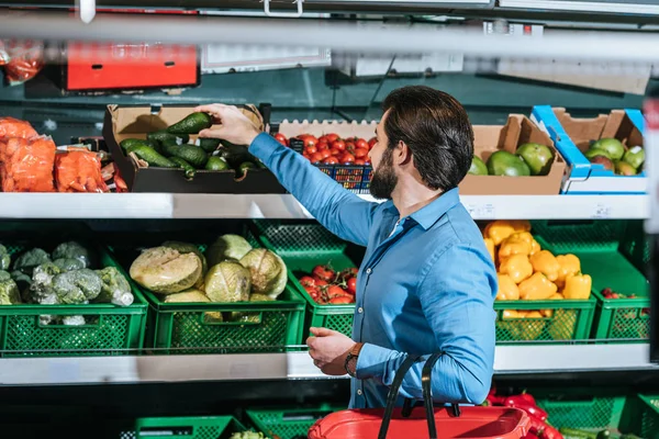 Hombre con cesta de la compra elegir verduras frescas en la tienda de comestibles - foto de stock