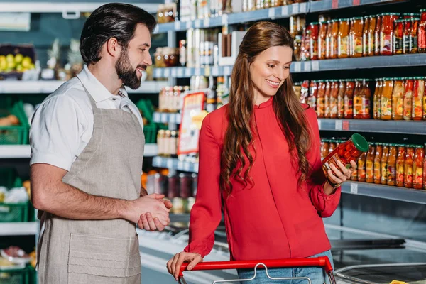 Retrato del asistente de tienda en delantal y de la compradora en hipermercado - foto de stock