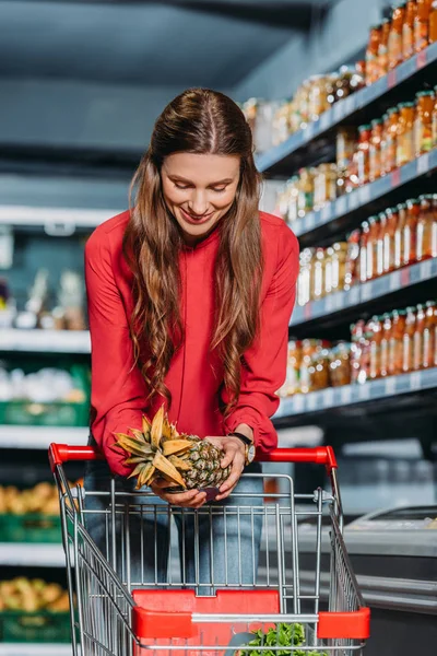 Mujer poniendo piña fresca en el carrito de la compra en el supermercado - foto de stock