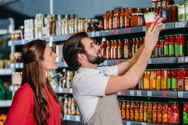 Portrait of shop assistant in apron helping female shopper in hypermarket — Stock Photo