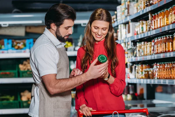 Retrato de assistente de loja em avental ajudando cliente feminino no hipermercado — Fotografia de Stock
