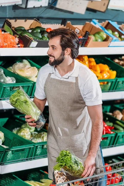 Assistente negozio sorridente organizzare verdure fresche in negozio di alimentari — Foto stock