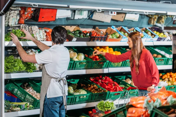 Vista lateral del asistente de tienda en delantal y comprador femenino en hipermercado - foto de stock