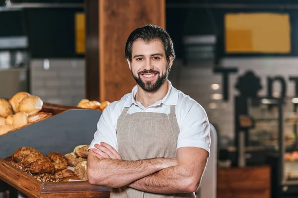 Portrait of smiling shop assistant in apron with arms crossed looking at camera in supermarket — Stock Photo