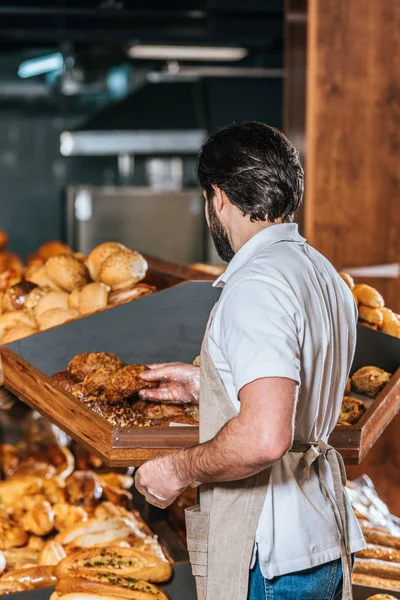 Vue arrière de l'employé de magasin masculin arrangeant le pain frais dans le supermarché — Photo de stock