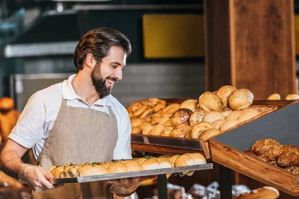 Sorridente commessa maschile che organizza pasticceria fresca nel supermercato — Foto stock