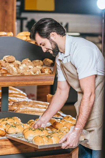 Asistente de tienda masculino sonriente organizando pastelería fresca en el supermercado - foto de stock