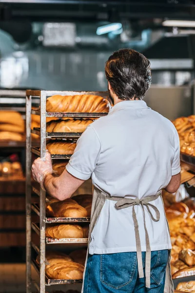 Vue arrière du magasinier dans le tablier organiser la pâtisserie fraîche dans le supermarché — Photo de stock