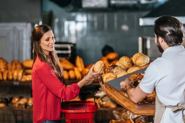 Shop assistant giving loaf of bread to woman with shopping basket in supermarket — Stock Photo