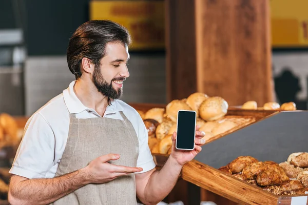 Portrait of smiling shop assistant showing smartphone with blank screen in supermarket — Stock Photo