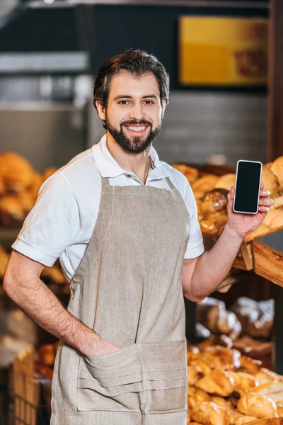 Portrait d'un assistant de magasin souriant montrant un smartphone avec écran blanc dans un supermarché — Photo de stock