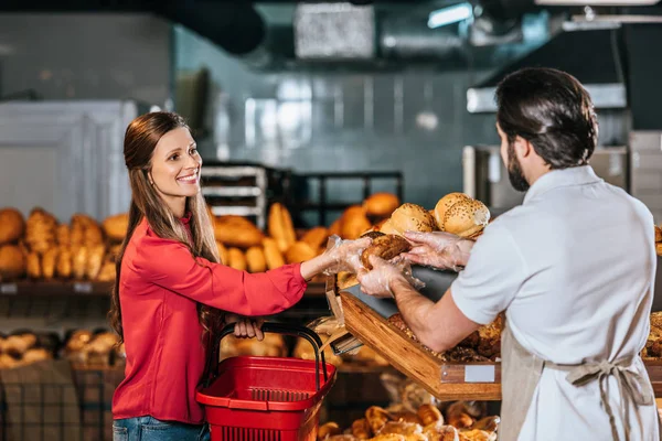 Verkäuferin gibt lächelnde Frau im Supermarkt ein Brot — Stockfoto