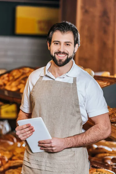 Portrait of smiling shop assistant with tablet looking at camera in supermarket — Stock Photo