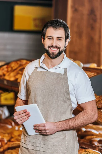 Retrato de sorrindo assistente de loja com tablet olhando para a câmera no supermercado — Fotografia de Stock