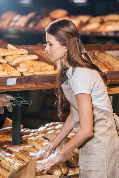 Vista lateral del asistente de la tienda la organización de panes en el mercado de compras - foto de stock