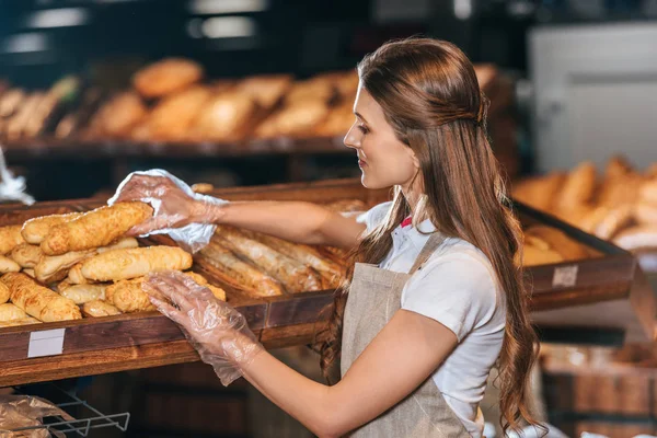 Vista lateral do assistente de loja organizando loafs de pão no mercado de compras — Fotografia de Stock