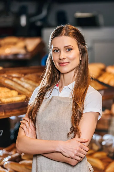 Portrait of smiling shop assistant in apron looking at camera in hypermarket — Stock Photo