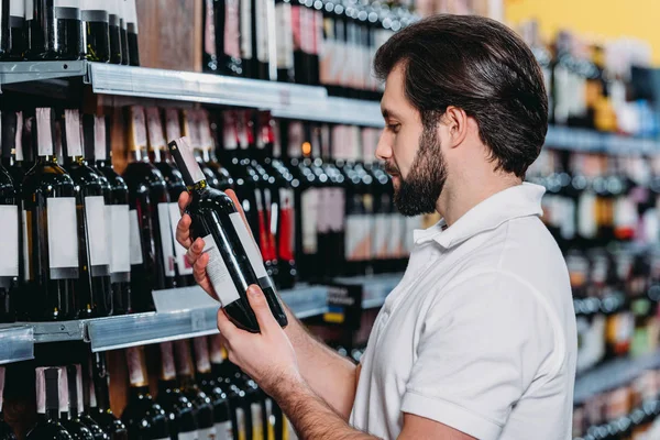 Asistente de tienda masculina que arregla el alcohol en el supermercado - foto de stock