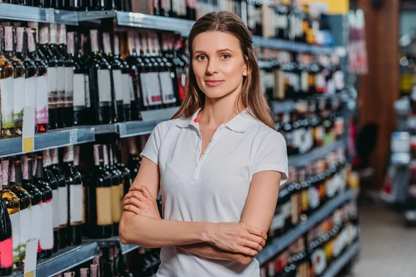 Retrato de mujer asistente de tienda con los brazos cruzados mirando a la cámara en el supermercado - foto de stock