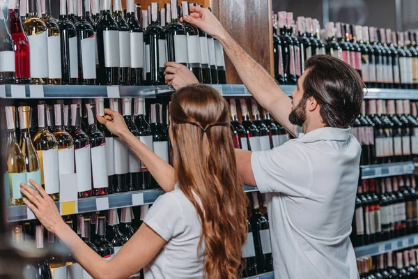 Vista lateral de los asistentes de tienda organizando botellas de vino en el hipermercado - foto de stock