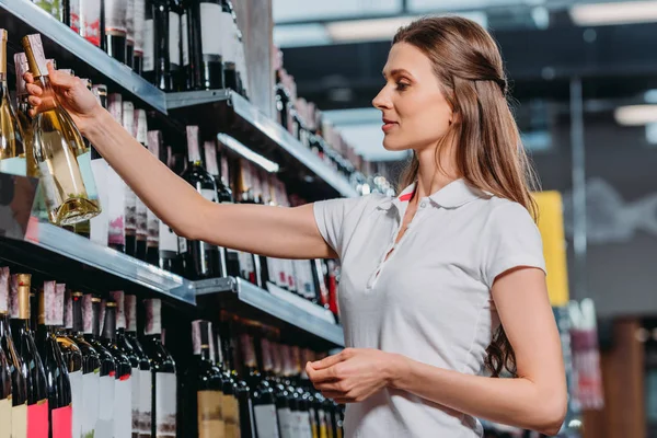 Side view of female shop assistant with bottle of wine in hypermarket — Stock Photo