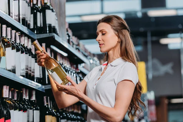 Side view of female shop assistant with bottle of wine in hypermarket — Stock Photo