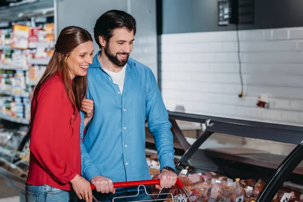 Casal feliz com compras carrinho compras juntos no supermercado — Fotografia de Stock