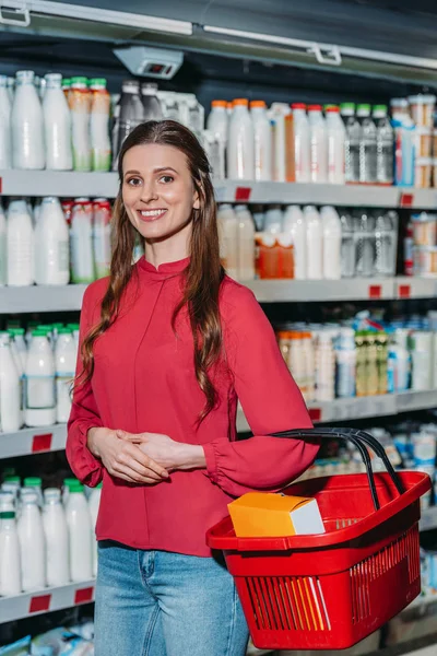 Retrato de mujer sonriente con cesta de la compra en el supermercado - foto de stock