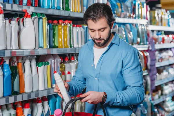 Retrato del hombre poniendo detergente en la cesta de la compra en el supermercado - foto de stock
